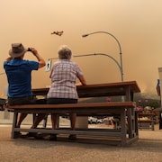 Un couple assis à une table observe un bombardier d'eau sous un ciel enfumé.