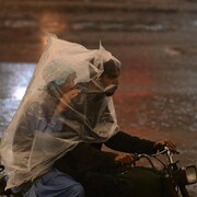 Deux Pakistanais roulent à moto dans une rue inondée, enveloppés d'un sac de plastique pour se protéger de la pluie.