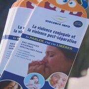 Une main tient une brochure de l'organisme Violence Info sur la violence conjugale.