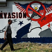 Un homme passe devant une fresque d'un aigle américain survolant le canal sur laquelle est écrit : « Non à l'invasion ».