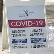 Une petite pancarte posée sur la neige sur laquelle il est écrit COVID-19, sur fond rouge.