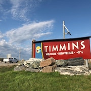 Une camionnette blanche passe près d'une pancarte qui souhaite la bienvenue à Timmins en trois langues.