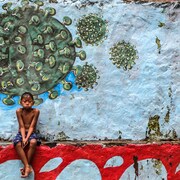 Un jeune garçon assis devant une murale représentant le coronavirus.