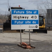 Un panneau qui annonce l'emplacement de la future autoroute 413 devant de l'équipement lourd à Woodbridge, en Ontario.