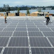 Deux personnes installent des panneaux solaires sur un grand toit plat.