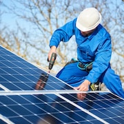 Un électricien installe des panneaux solaires sur le toit d'une résidence.