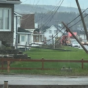 Des poteaux d'électricité brisés devant des maisons.