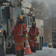 Des employés d'Hydro-Québec en train de marcher près d'un camion. Il y a de la neige au sol.