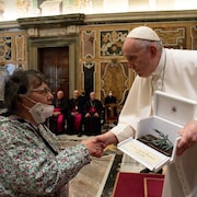 Le pape tient dans une main un écrin qui contient une sculpture et serre de l'autre main celle d'une femme.