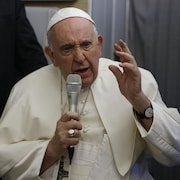 Le pape, assis dans son avion, avec un micro à la main.