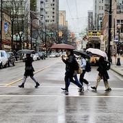 Des gens, avec des parapluie, traversent la rue à une intersection.