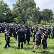 Des dizaines de policiers restent aux aguets. Au loin, on voit des dizaines de manifestants avec des affiches.