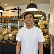 Un homme devant un présentoir de pain d'une boulangerie. 