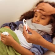 Une infirmi&egrave;re prend la temp&eacute;rature d'une fillette allong&eacute;e dans un lit.