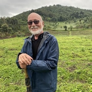 L'artiste pose en souriant devant des collines verdoyantes.