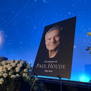 Une affiche sur laquelle on peut lire À la mémoire de Paul Houde, près d'un bouquet de fleurs.