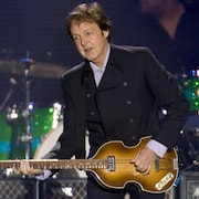 Paul McCartney sourit tout en jouant de la guitare lors d'un concert.