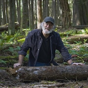 Paul Stamets agenouillé devant un tronc d'arbre dans une forêt.