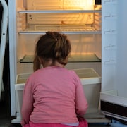 Une fillette assise devant un frigo vide.