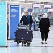 Deux voyageurs près d'un kiosque d'enregistrement de bagages à l'aéroport Pearson.