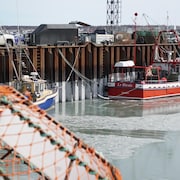 Un bateau amarré au quai avec une cage de crabe en avant-plan.