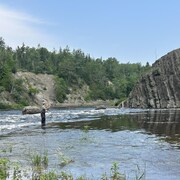 Un pêcheur les pieds dans l'eau lance sa ligne dans la rivière Rimouski. 