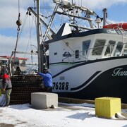 Un bateau de pêche est à quai, des hommes installent des paniers de pêche à crabe à une grue.