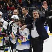 Des joueurs des deux équipes posent pour une photo. Un entraîneur ukrainien envoie la main au public. 