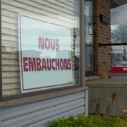 Une enseigne « Nous embauchons » est placée en évidence derrière la fenêtre d'une entreprise.