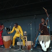 Trois hommes jouent des percussions sur une scène.