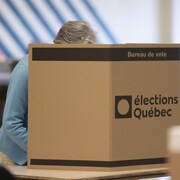 Une femme vote derrière un panneau dans un bureau de vote.