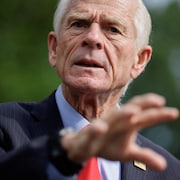 Peter Navarro, vêtu d'un veston sombre et d'une cravate rouge, fait un geste de la main tout en parlant.
