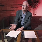 Un homme consulte des documents sur un fauteuil. 