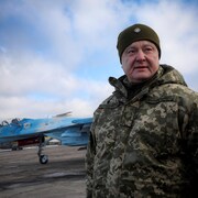 Petro Porochenko pose en habit de camouflage sur un tarmac, un avion militaire se trouve derrière lui.