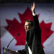 Pierre Poilievre livre un discours devant un drapeau canadien. 
