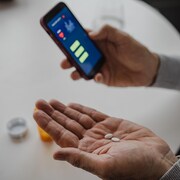 Plan serré des mains d'une personne qui tiennent des pilules et d'un téléphone. 