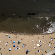 Une photo aérienne de la plage de Verdun, où plusieurs personnes sont installées sur le sable et où d'autres personnes se baignent dans de l'eau brunâtre, le 30 juin 2025.