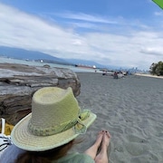 Une femme est assise sur la plage de Locarno avec au loin un navire marchand et la ville de Vancouver.