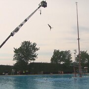 Une femme plonge du haut d'une grue dans une piscine. 