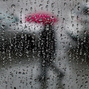 Une silhouette avec un parapluie aperçue à travers une vitre couverte de gouttes de pluie.