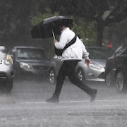 Un piéton marche sous un parapluie dans la rue sous une pluie abondante. 