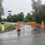 Des cônes orange et une pancarte qui bloque la route. Sur celle-ci, il est indiqué « circulation locale seulement ». Trois pompiers se trouvent plus loin. 
