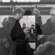 Addesse Haile à gauche et Latif Murji à droite sur le quai d'une station de métro à Toronto. À l'avant-plan, des passagers dans un wagon de métro.