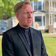 Dominic Cardy en entrevue devant une grande maison. 
