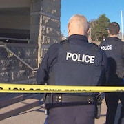 Deux policiers en uniforme, de dos, derrière le cordon jaune qui délimite une scène de crime.