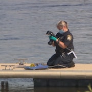 Une policière prend une photo d'un objet sur un quai.