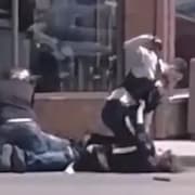 Un agent de la GRC lève le poing au-dessus de la tête d'un homme plaqué au sol lors d'une arrestation. À côté d'eux, un autre homme est accroupi au-dessus d'un autre individu.
