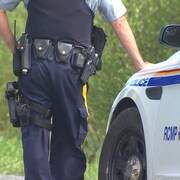 Un policier de la GRC, la main posée sur sa voiture de patrouille.