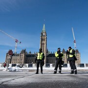 Des agents de protection du Service de protection parlementaire devant le parlement du Canada, en hiver.