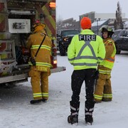 Trois pompiers de dos discutent derrière un camion de pompier, à Bonnyville, en Alberta